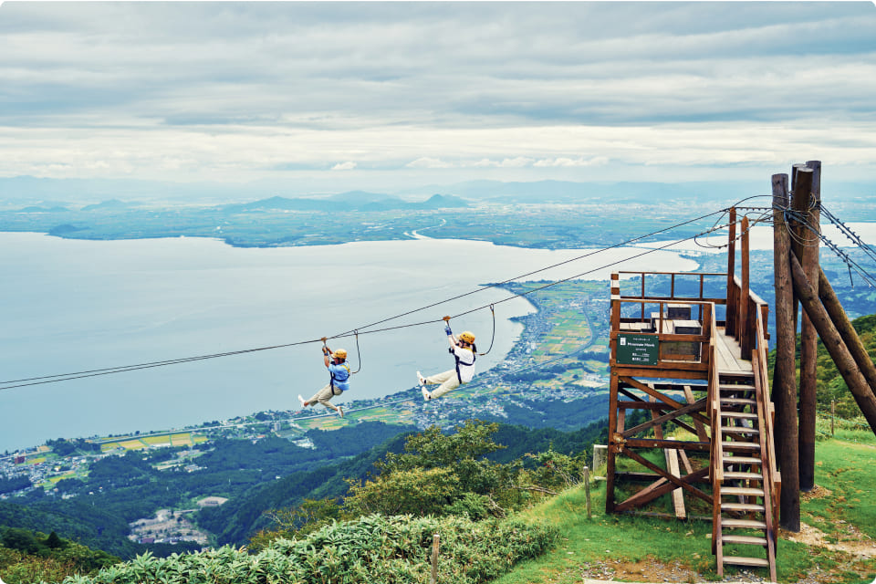 緑豊かな山々を背景に、ジップラインを楽しむ人々と湖の絶景。