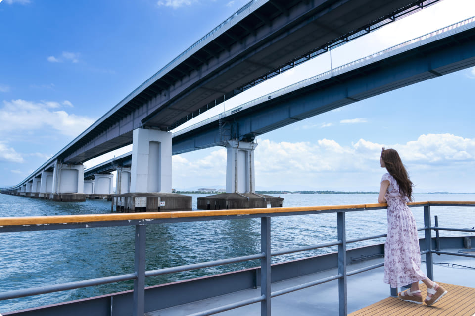 湖をまたぐ壮大な橋と、手すり越しに景色を眺める女性。