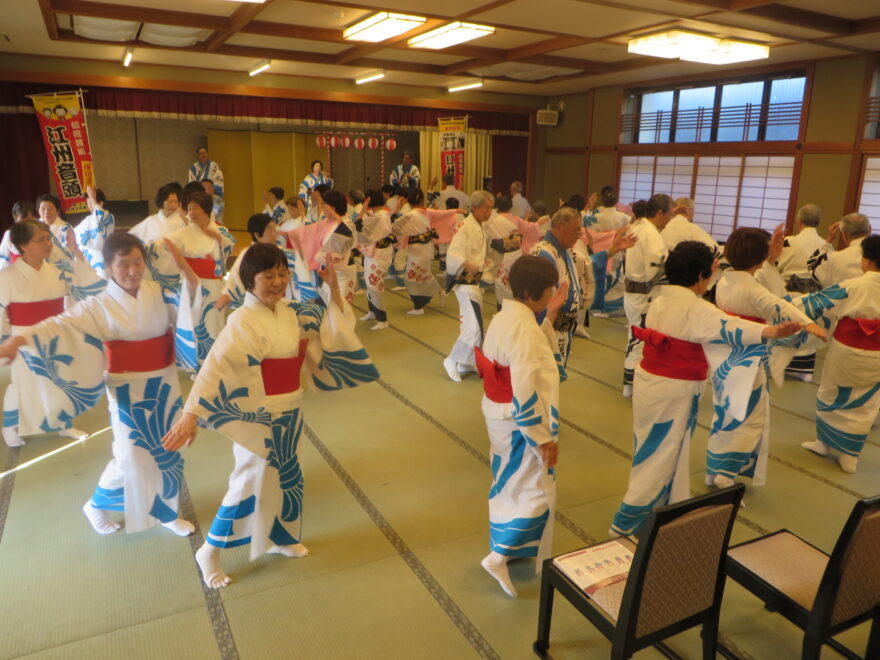 室内で浴衣姿の人々が円形になり、伝統的な踊りをしている様子。