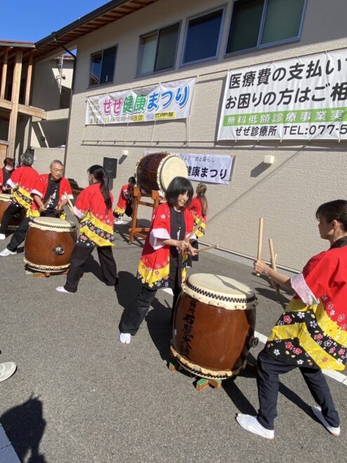 屋外で和太鼓を演奏しているグループ。明るい日差しの中、真剣な表情で演奏している。